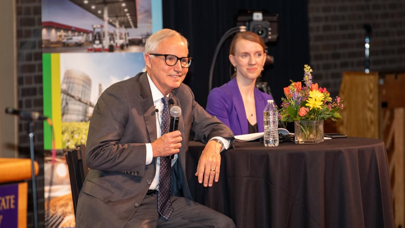 a person in a suit and tie sitting at a table with a microphone