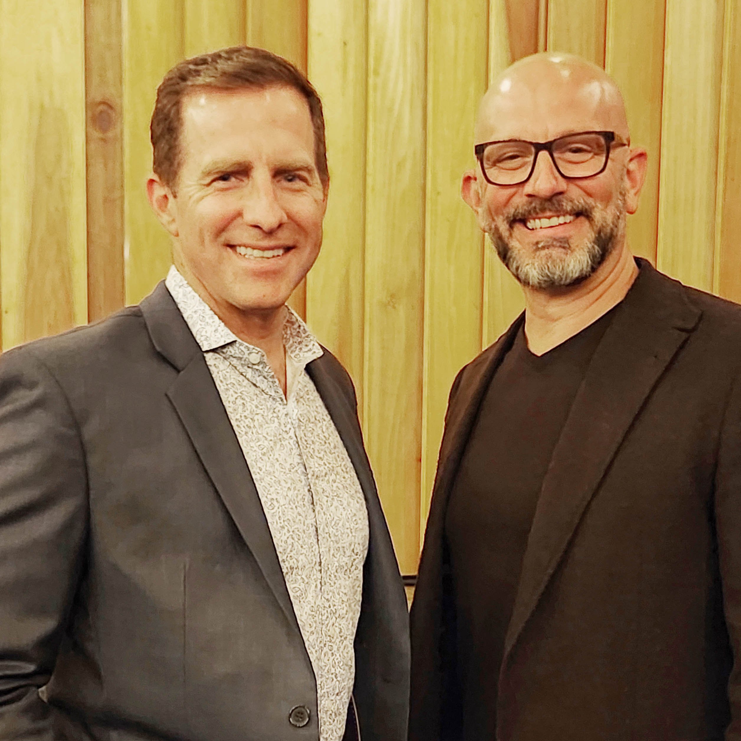 Kevin Meyer and Michael Dolan pose together in suits and smiling at the camera.