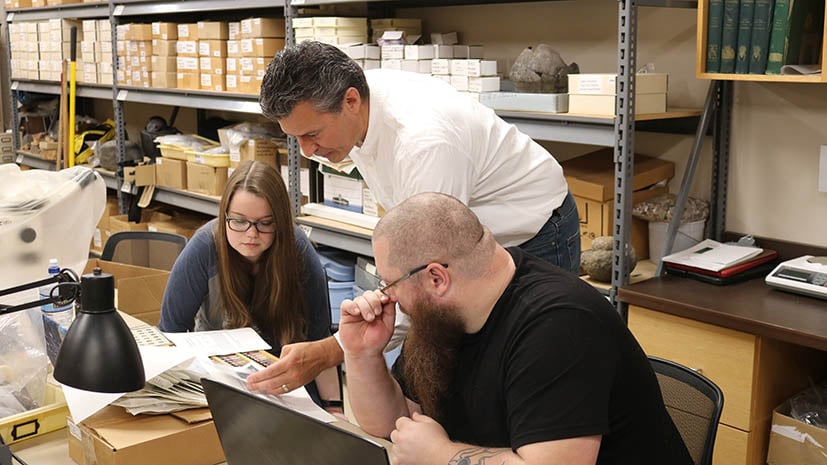 professor helping two students with artifacts for a museum