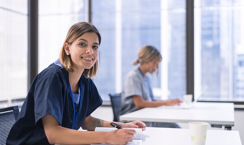 Women looking at camera, sitting at a desk.