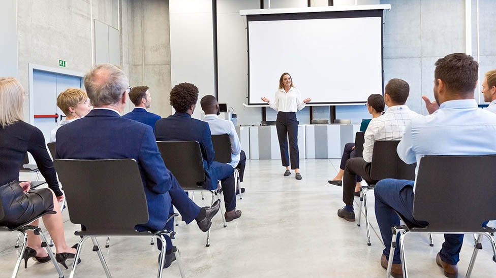 female business leader giving a presentation in front of a group of business people