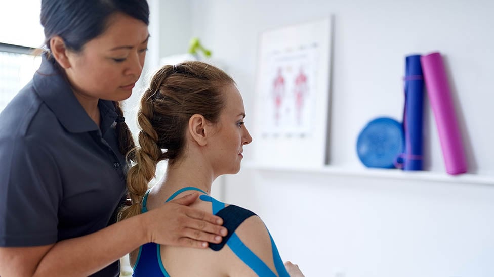 An Athletic Trainer working with a patient in a clinic setting. She is helping to tape her shoulder and arm
