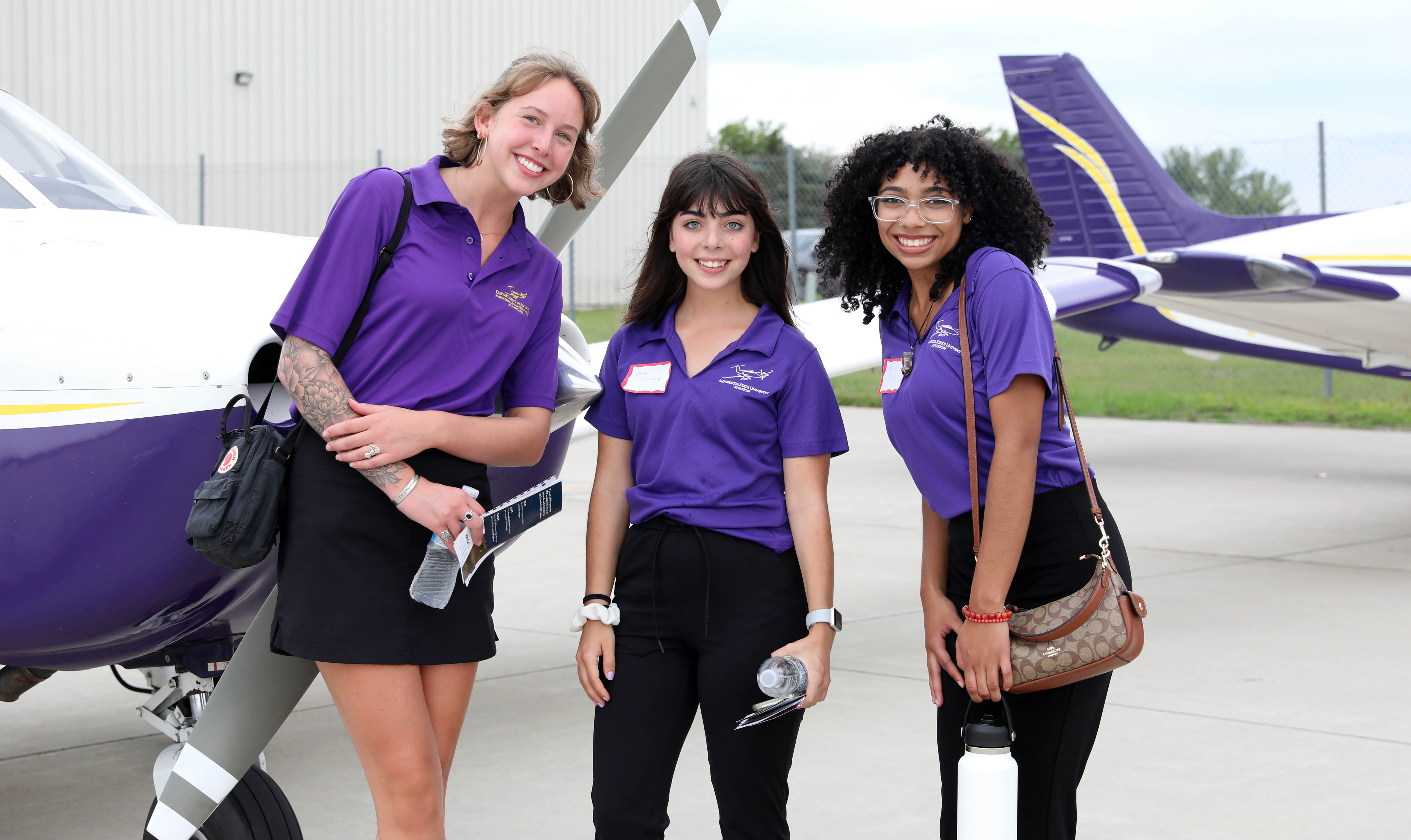 three female students in purple MSU tee shirts posing in front of two airplanes