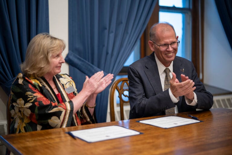 President Inch and the President McDonald sitting at a table clapping hands and smiling