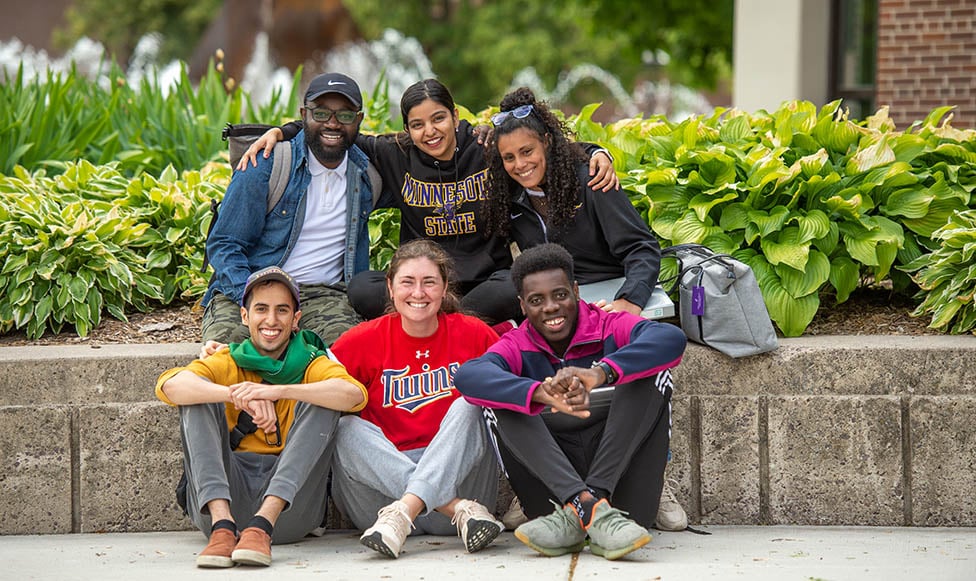 Six students sitting outside on campus posing for the camera