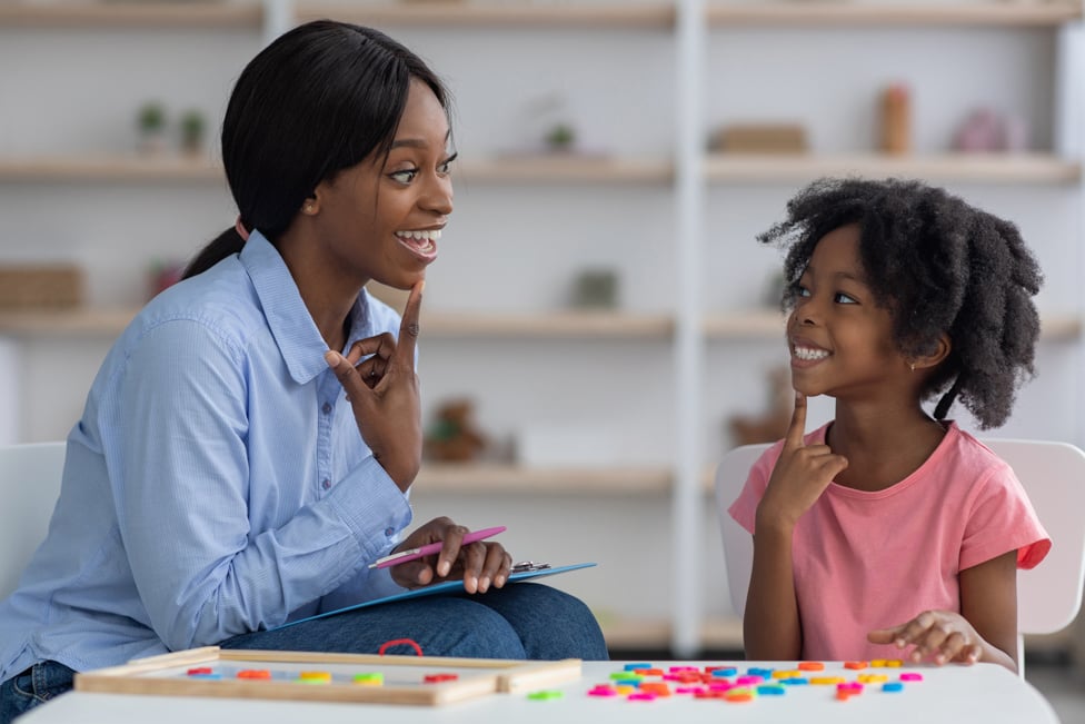 Speech therapist and child sitting in office, helping child say letters.