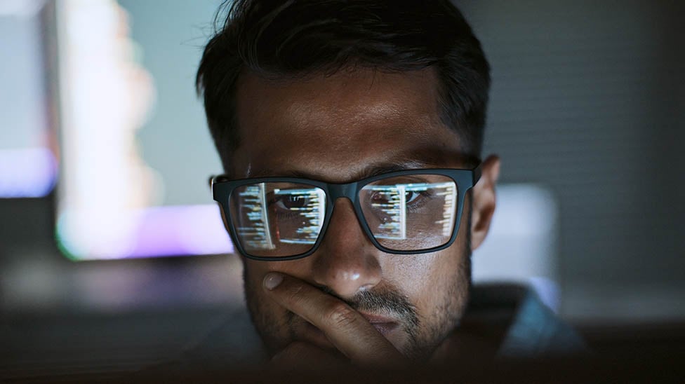 male looking at the computer screen with the screen reflecting on his glasses