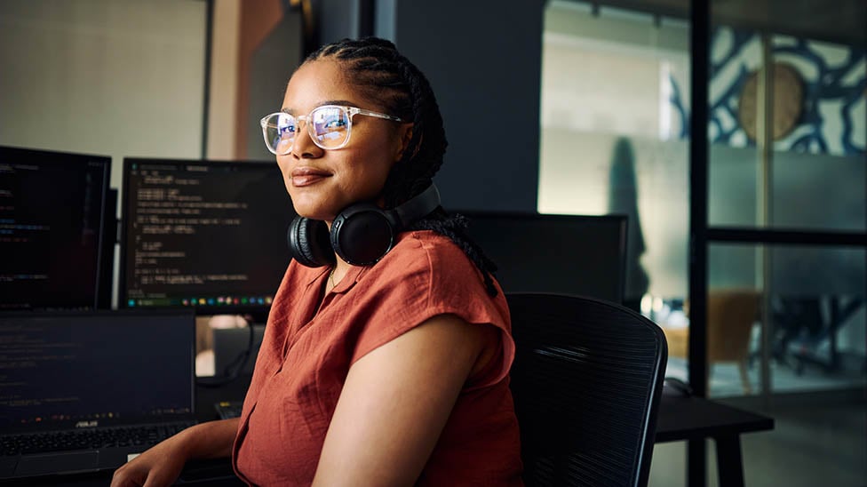 female student with headphones sitting in front of a computer with code on it