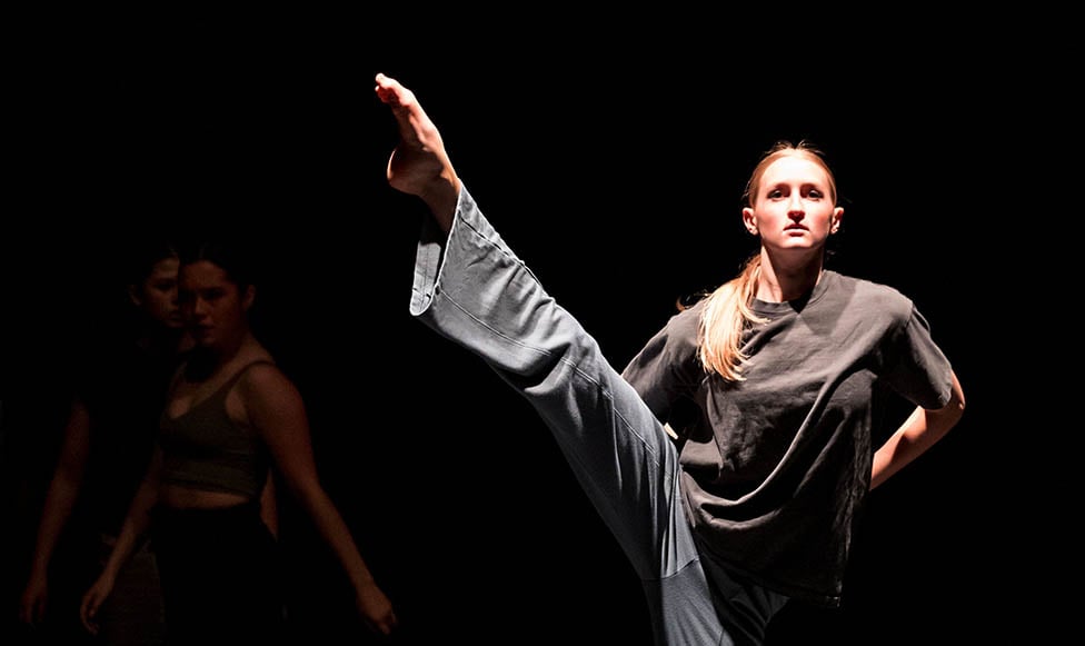 one student on stage in a dance pose and a dark stage with the spotlight on the dancer