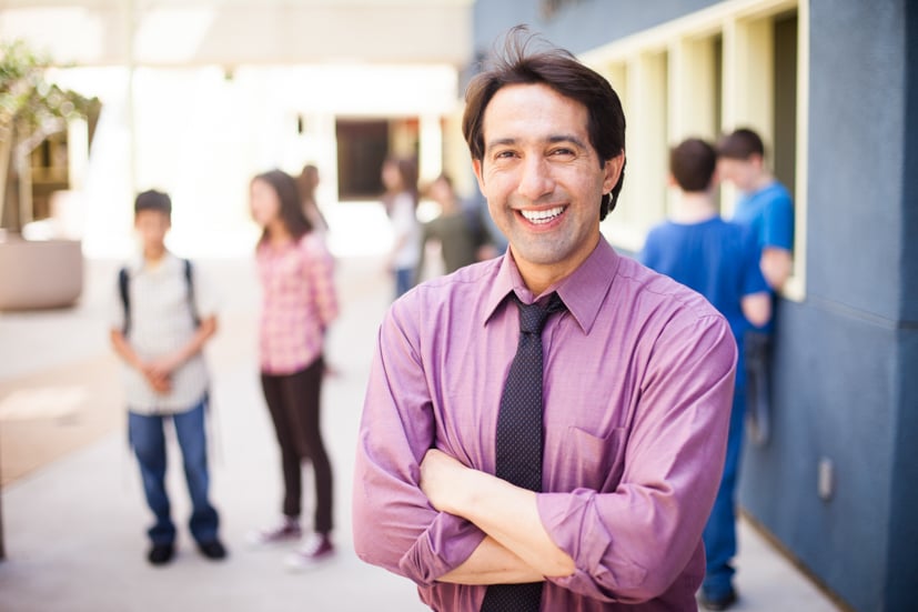 Man standing with arms crossed smiling, wearing a button down shirt.