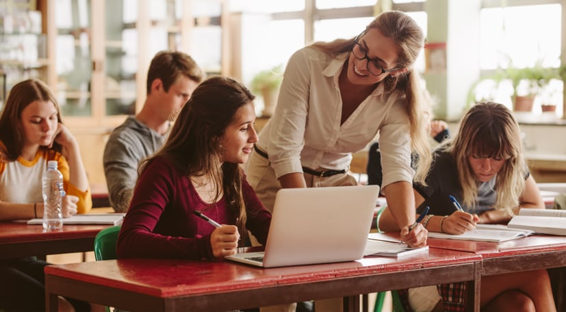 Teacher helping student at desk on a computer.