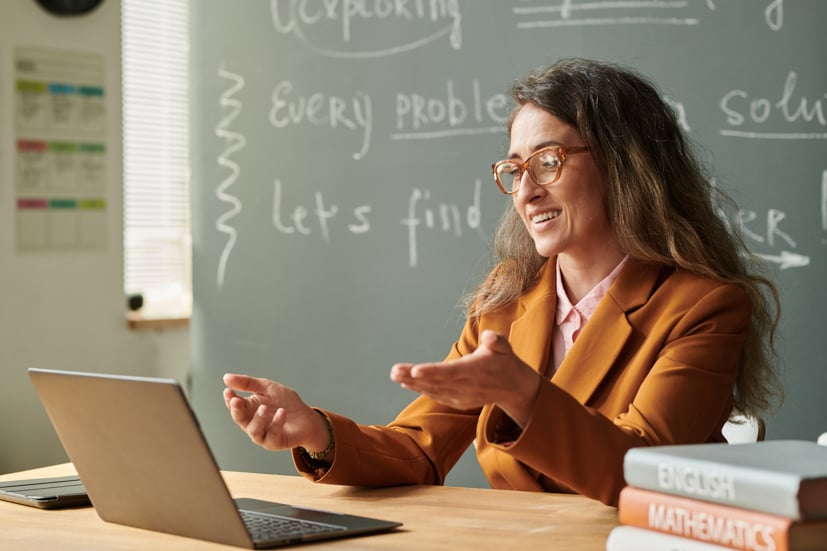 Women teacher looking at computer sitting at a desk and talking.