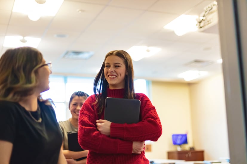 Girl student holding computer, smiling and walking out of classroom.