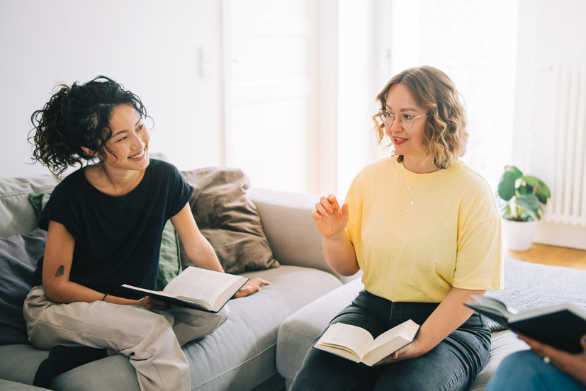 Two girls holding books having a conversation.