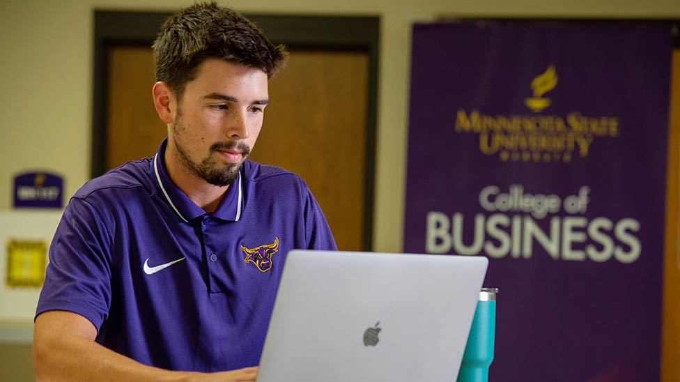 student on laptop with the College of Business sign in the background