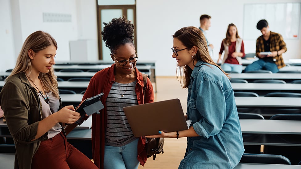 group of 3 women looking at laptop and tablet with another group of 3 students behind them