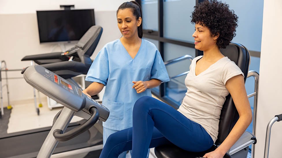 A Exercise Science professional in scrubs helping a female patient on a recumbent bike for cardiac rehabilitation