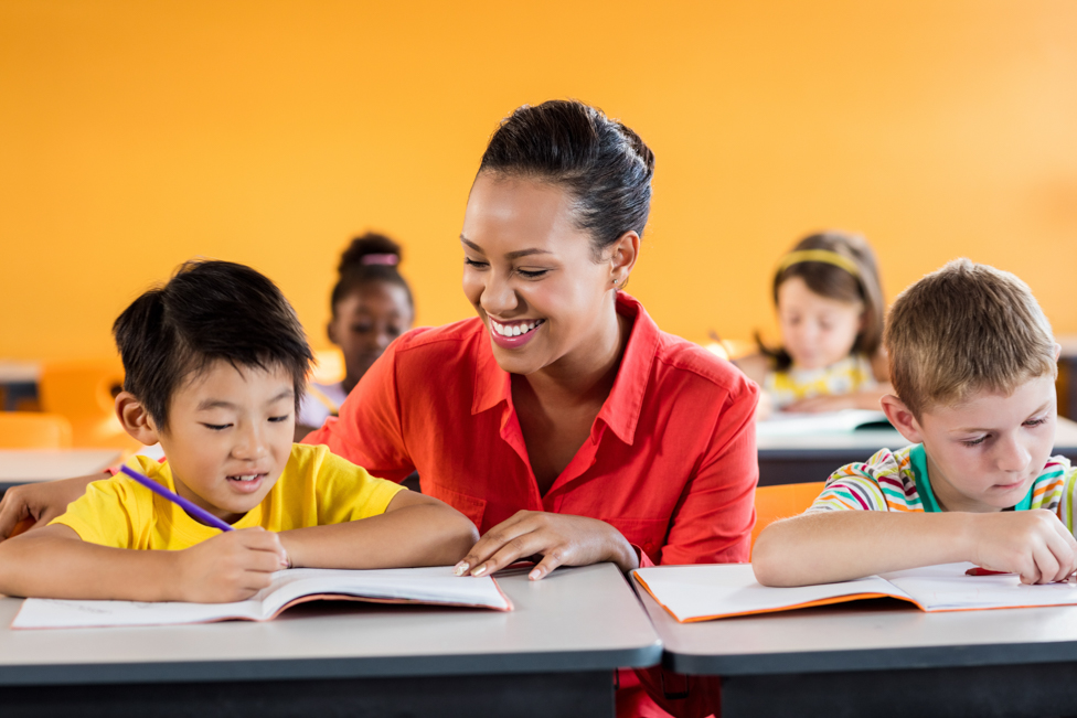 Elementary school teacher helping student read. 