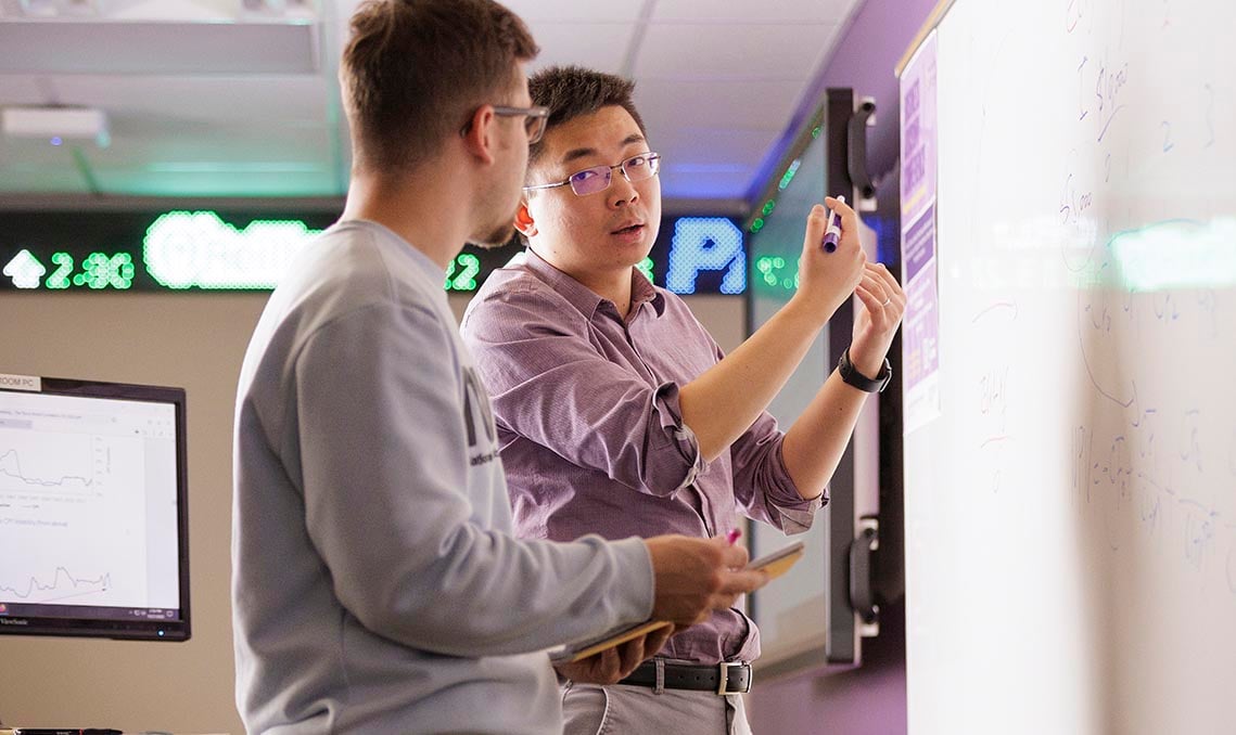 Image of professor with student explaining and writing on the white board.