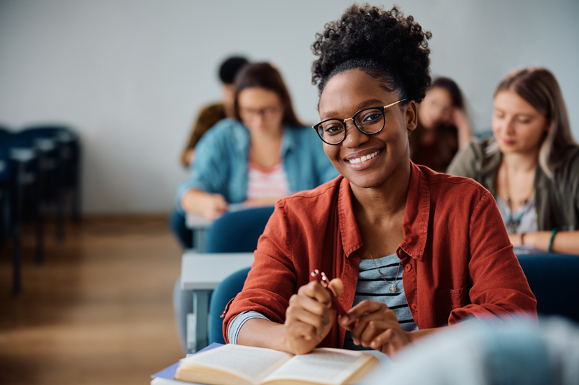 Woman sitting in a classroom with book open, smiling.