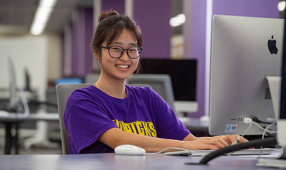 MSU student working at a computer in a library, smiling