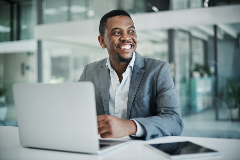 Man in a suite sitting my his computer smiling.
