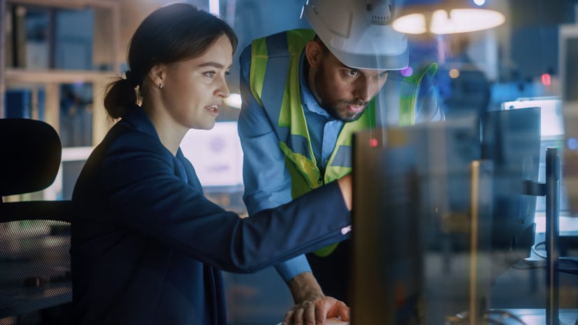 Woman pointing at computer screen, man with construction hat looking at a screen.