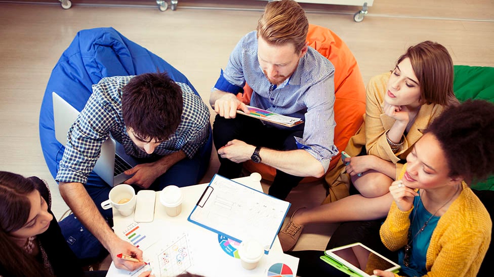 Aerial view of students gathered around a table looking at charts for a group project.