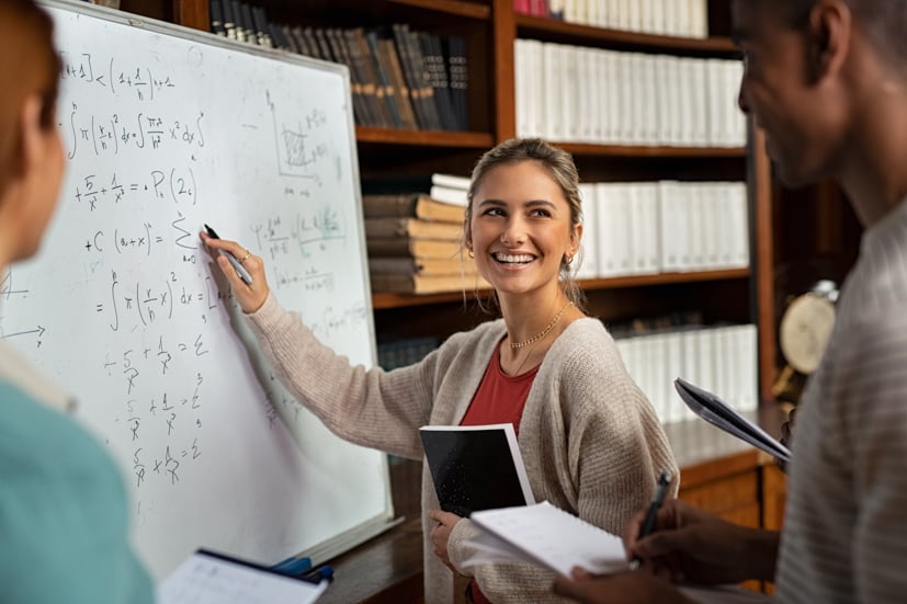 Woman pointing at a whiteboard with math equations on it.
