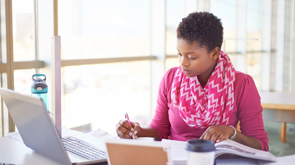 woman writing in her notebook with laptop nearby