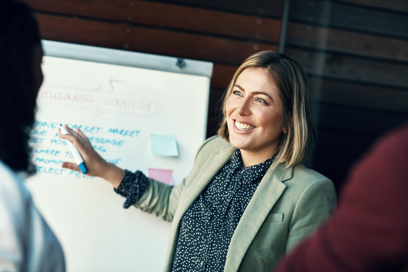 Women smiling and pointing at a board with notes.