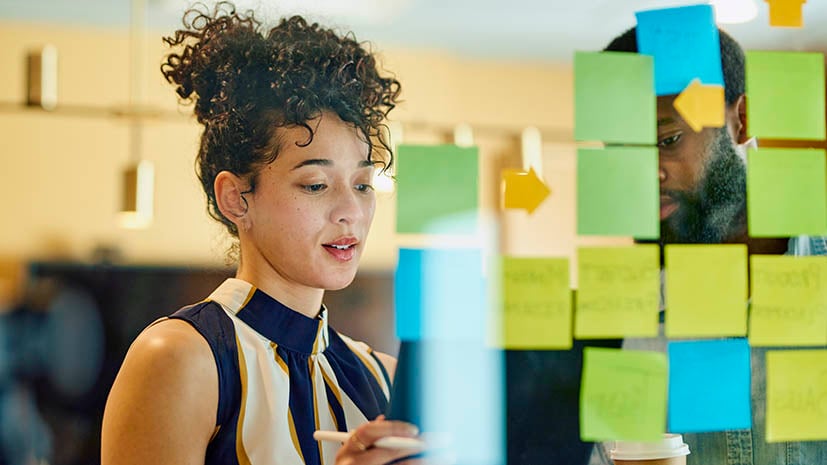 A woman in a board room putting sticky notes on the board to lead a group through a project. 