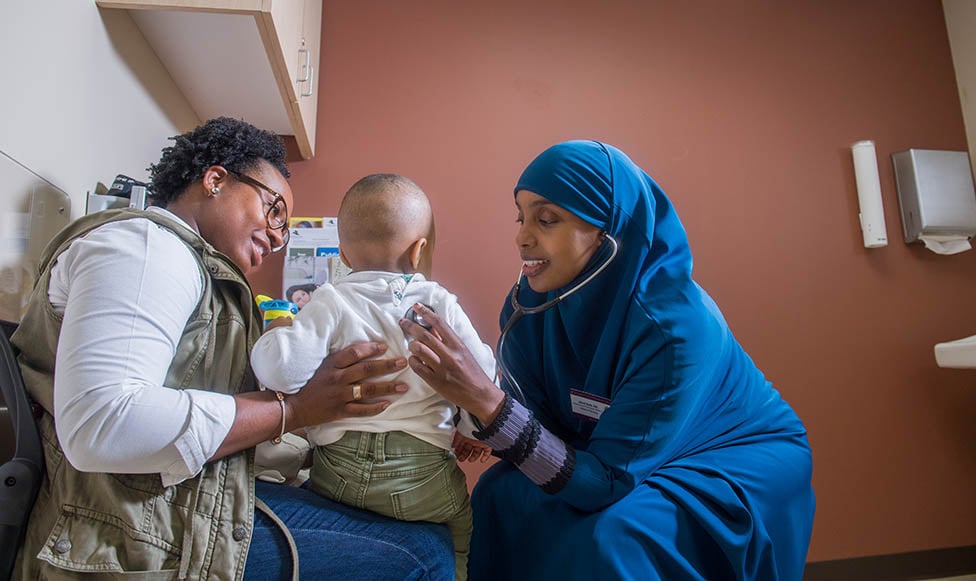 Nurse listening to small boys using a stethoscope while the child is sitting on his parent's lap