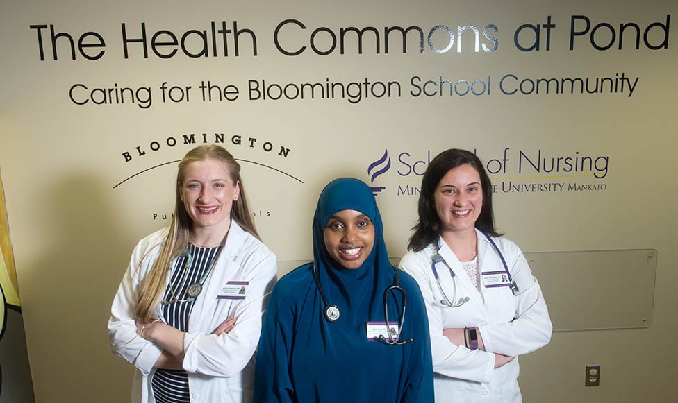 three student nurses standing in front a nursing sign. 