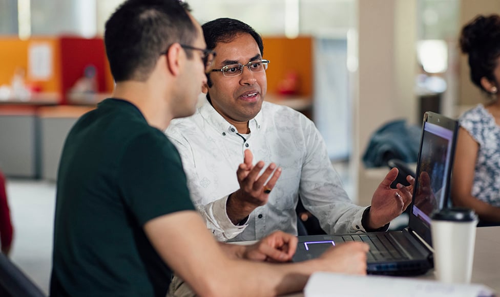 Teacher talking to college student by a computer.
