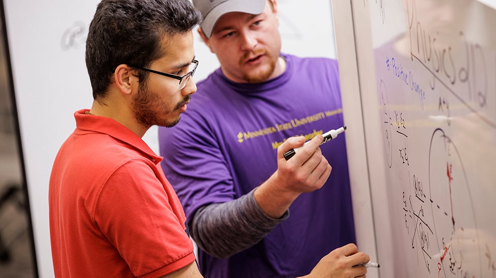 Two students working together on a white board.