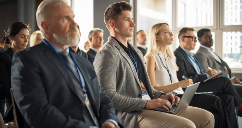 Group of people in a room, at an event, taking notes on computer or listening.