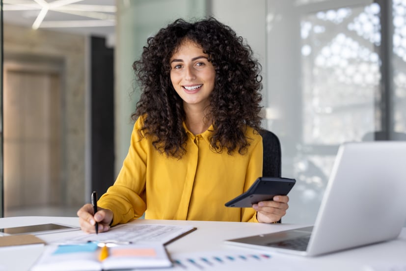 Women working at desk with calculator and computer.