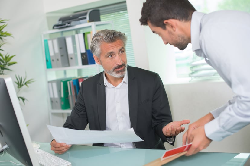 Two men talking to each other in an office at a desk.
