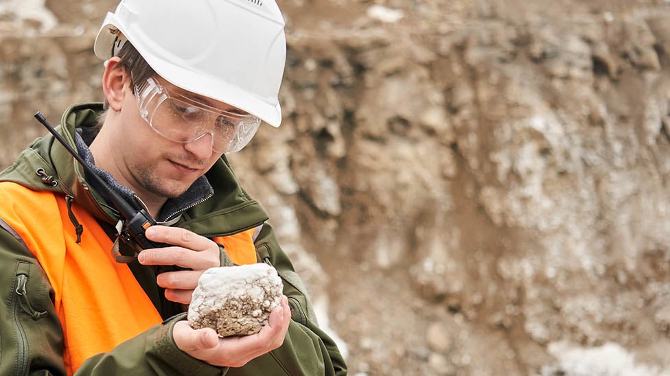 student holding a rock and looking at it while wearing a hard hat and reflective vest