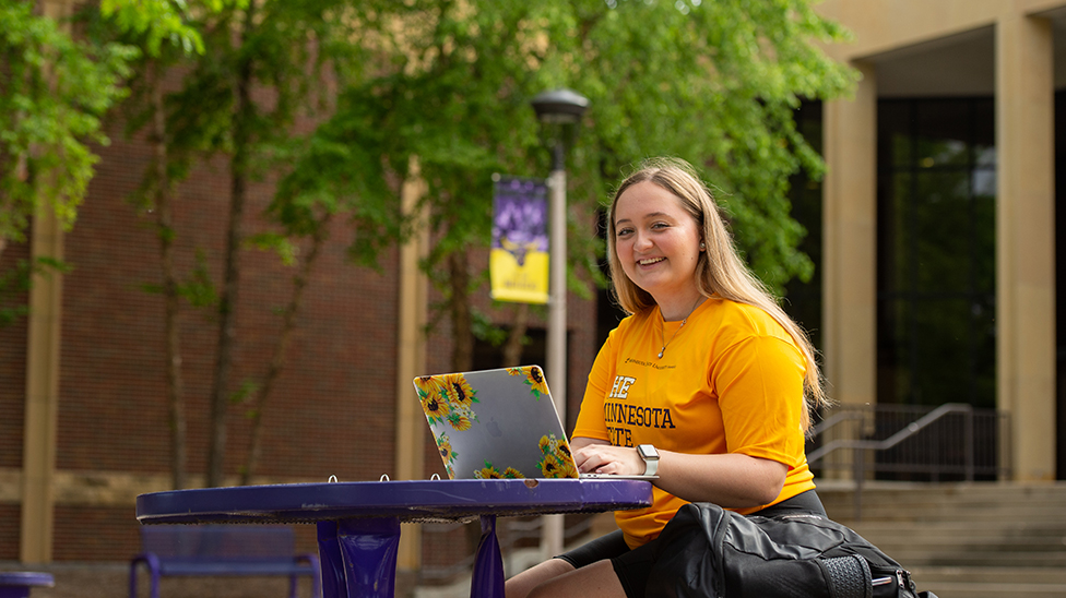 student sitting outside on campus on her laptop