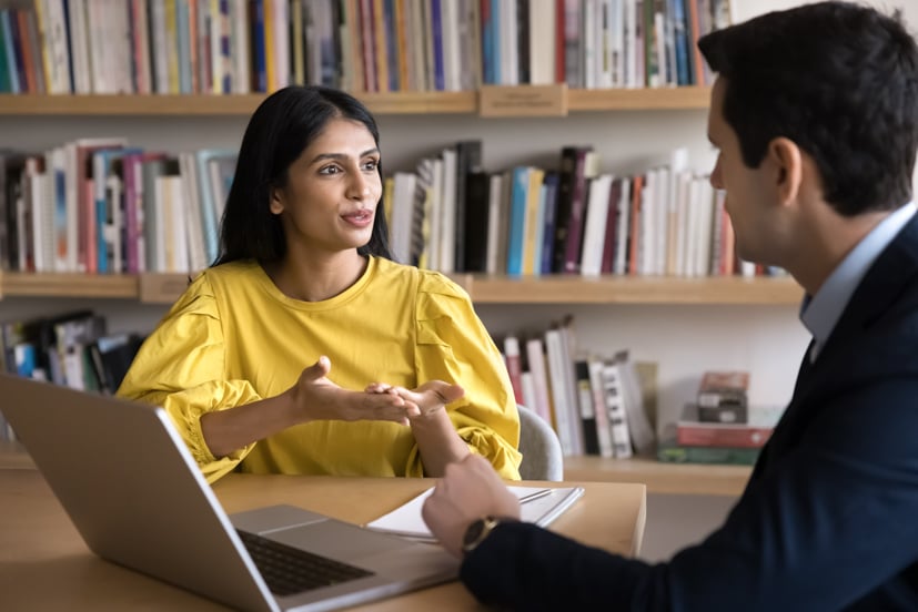 Women talking to a man at a desk with her hand outstretched.