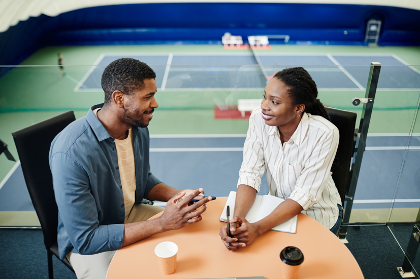 Man and woman talking at a table with coffee in an office.
