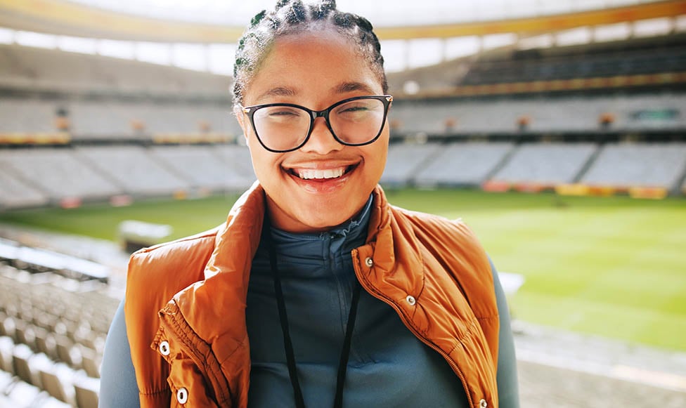 A diverse female sports management professional posing in an empty stadium