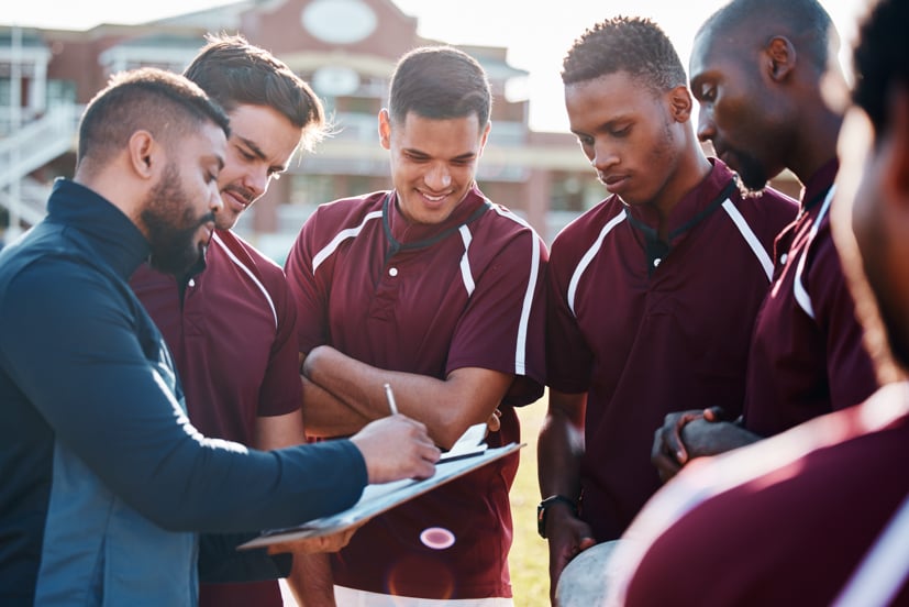 Coach talking to athletes on the field, in a circle.