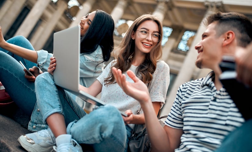 Group of students talking by a computer, sitting outside.