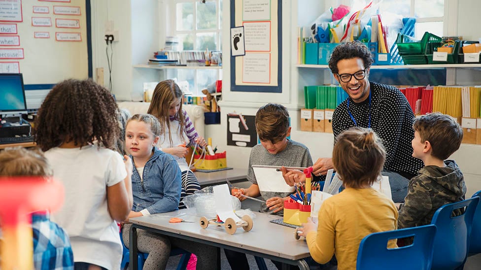 diverse male teacher at a table with young school aged children learning and laughing