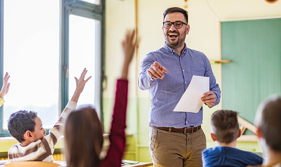 Male teacher smiling and pointing at a student in the classroom to talk.