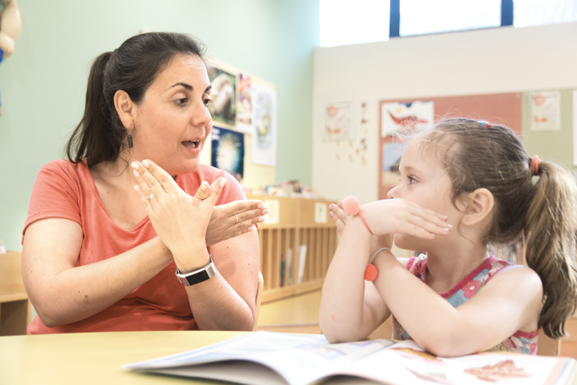 Teacher and child working on sign language at table. 