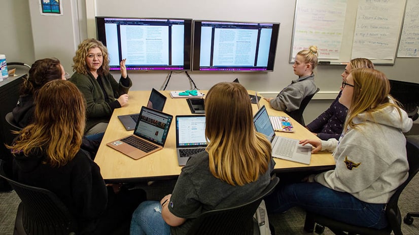 special education teacher sitting around a computer screen talking with students